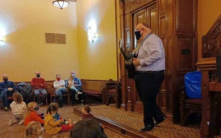 Cantor Hyman with a guitar in front of a group of toddlers